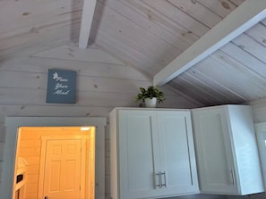 A room with white wooden walls and ceiling, a white door, and a cabinet with two doors. There is a sign on the wall and a potted plant on top of the cabinet.