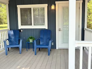 A porch with two blue chairs, a small table with a plant, and a white door.