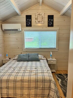 Een slaapkamer met een bed, een raam met zonwering, een airconditioner en twee speakers bevestigd aan de muur.
