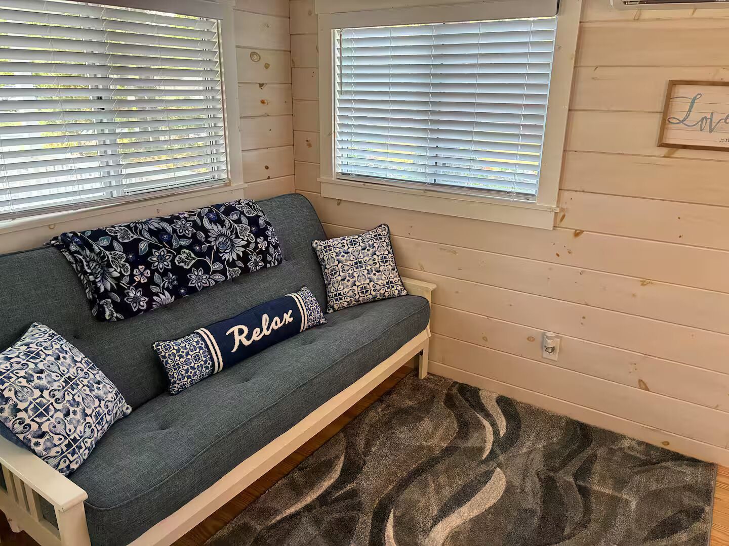 Een kamer met een grijze bank, gekleurde kussens en een vloerkleed.