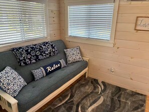 Een kamer met een grijze bank, gekleurde kussens en een vloerkleed.