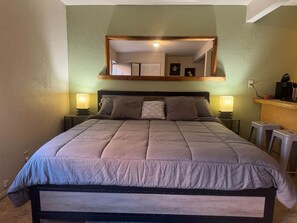 A bed with a headboard, two bedside lamps, and a mirror above the bed.