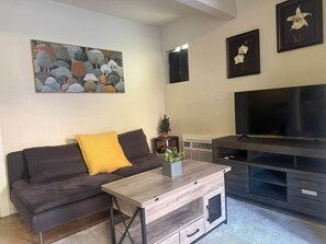A living room with a sofa, a coffee table, a TV, and framed artwork on the wall.