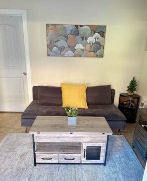 A living room with a sofa, a coffee table, a painting, and a small plant. - Trail Head Studio Suite (Village of Oak Creek)