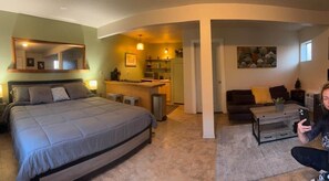 A bedroom with a large bed, a sitting area with a coffee table, and a kitchen in the background.