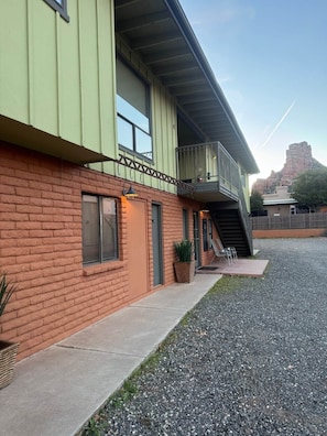 A two-story building with a brick facade, a balcony, and a gravel driveway.