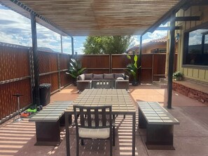 En udendørs patio med overdækket siddeområde, et bord og en bænk.