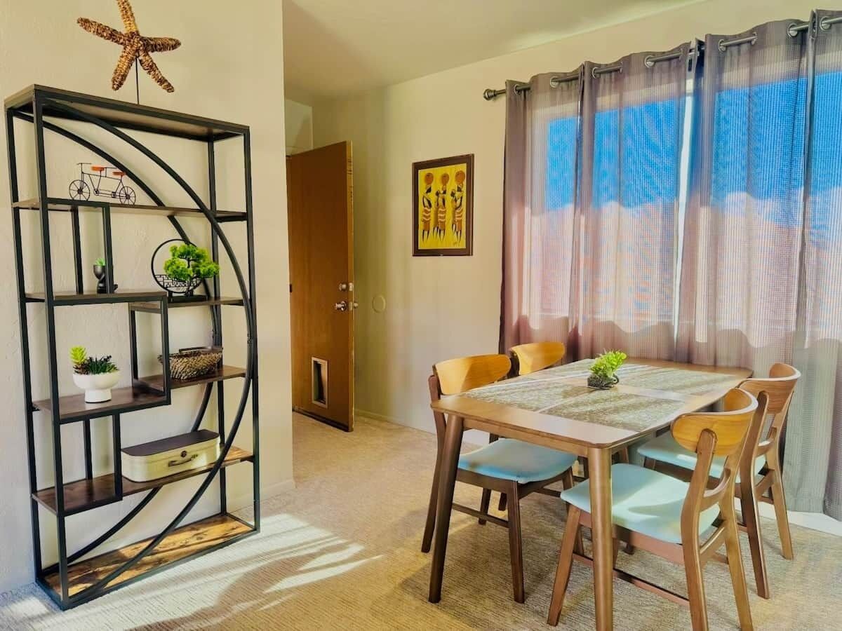 A dining area with a table and chairs, a decorative metal shelf with plants, and a door leading to another room.