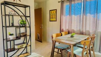 A dining area with a table and chairs, a decorative metal shelf with plants, and a door leading to another room.