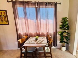 A dining area with a table and chairs, a potted plant, and a window with curtains.