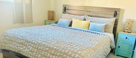 Una cama con cubrecama acolchado, dos mesitas de noche con adornos y un cuadro en la pared.