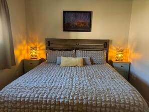A neatly made bed with a textured blanket, a framed picture above it, and two bedside lamps on either side.