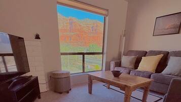 A living room with a television, a sofa, a coffee table, and a large window with a view of a landscape.