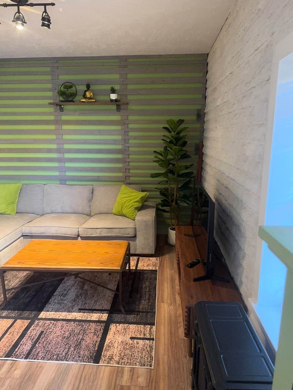 A living room with a sofa, coffee table, and a television. There is a green wall with horizontal lines and a plant.