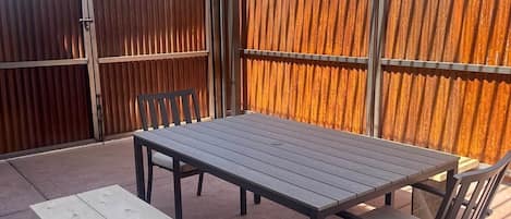 Un patio al aire libre con una mesa y sillas, un banco de madera y una valla metálica.