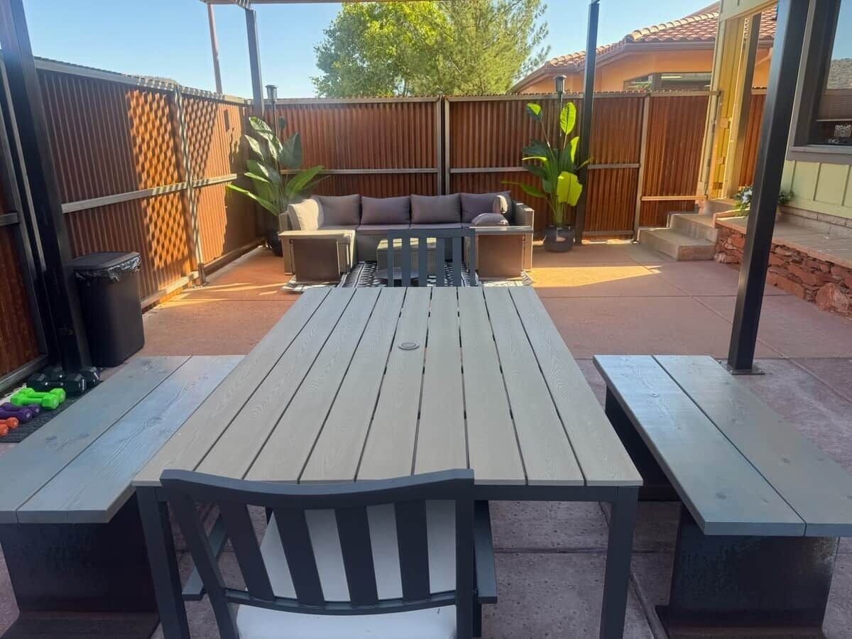 Une terrasse extérieure avec une table et des bancs en bois, un coin salon avec des coussins et une clôture en bois.
