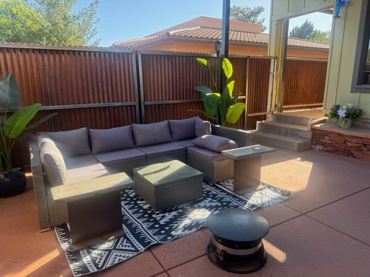 An outdoor patio with a sectional sofa, two side tables, and a round ottoman.