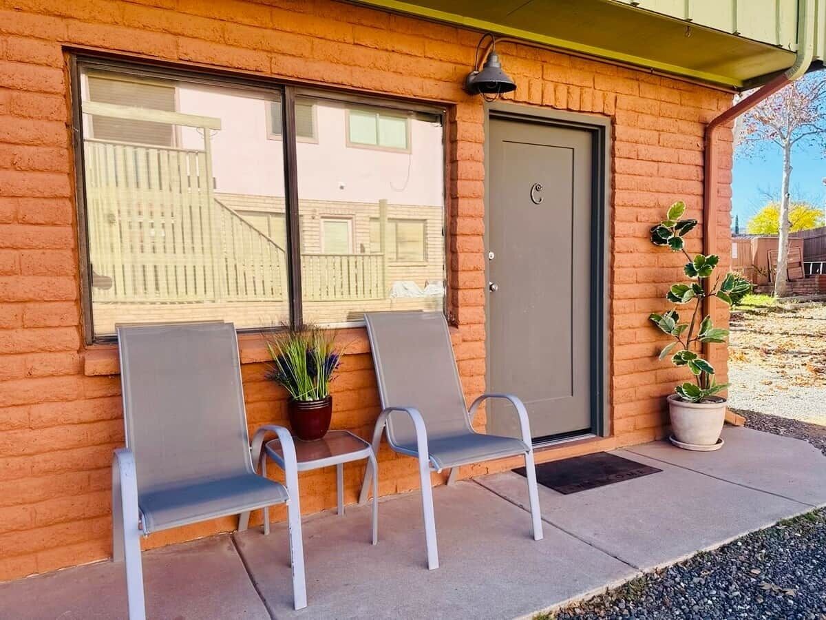 A building with a brick facade, a door, and two metal chairs with cushions.