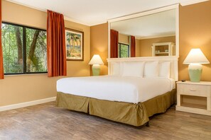 Een hotelkamer met een bed, twee bedlampen, een grote spiegel en een raam met gordijnen.