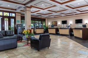 Een hotel lobby met een receptiebalie, een zithoek en een groot raam met uitzicht op palmbomen.