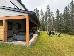 A wooden deck with a hot tub, outdoor seating, and a grill area. - Nature Getaway & Spa | Conifer (Notre-Dame-de-la-Merci)