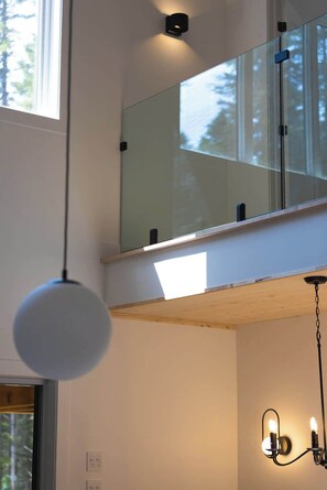 A room with a large window, a hanging light fixture, and a wall-mounted light fixture. - Nature Getaway & Spa | Conifer (Notre-Dame-de-la-Merci)