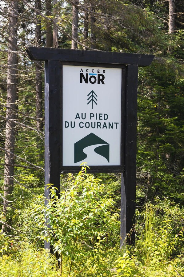 A sign with 'ACCES NOR' and 'AU PIED DU COURANT' text, surrounded by greenery. - Nature Getaway & Spa | Conifer (Notre-Dame-de-la-Merci)