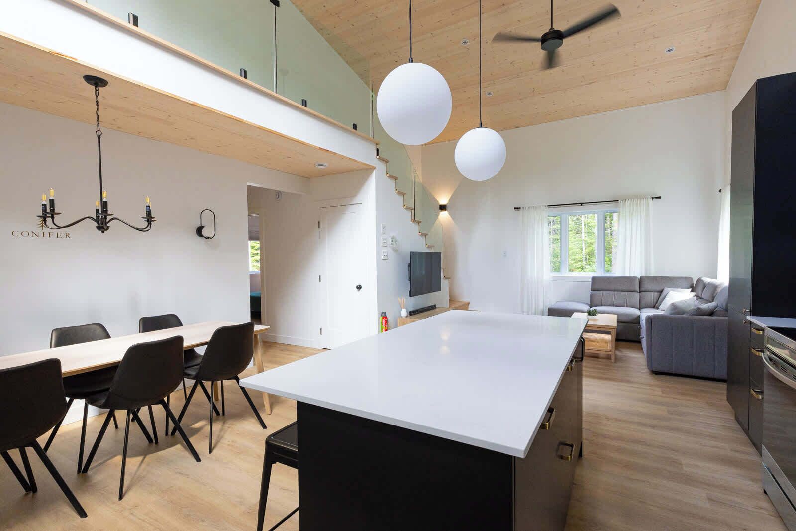 A modern kitchen with a central island, dining area with chairs, a sofa, and a TV.