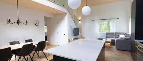 A modern kitchen with a central island, dining area with chairs, a sofa, and a TV.