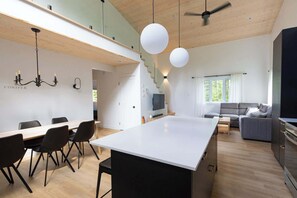 A modern kitchen with a central island, dining area with chairs, a sofa, and a TV. - Nature Getaway & Spa | Conifer (Notre-Dame-de-la-Merci)