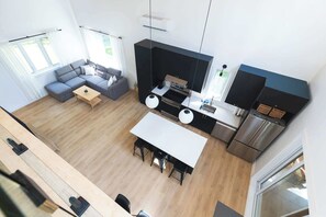A modern kitchen with a central island, a dining area with a white table, and a gray sofa. - Nature Getaway & Spa | Conifer (Notre-Dame-de-la-Merci)
