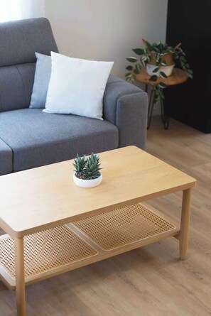 A room with a grey sofa, a wooden coffee table with a small plant, and a round side table with a potted plant. - Nature Getaway & Spa | Conifer (Notre-Dame-de-la-Merci)