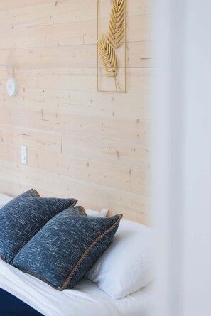 A bed with two pillows, a wooden wall, and a decorative leaf pattern. - Nature Getaway & Spa | Conifer (Notre-Dame-de-la-Merci)