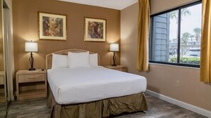 Een hotelkamer met een groot bed, twee nachtkastjes met lampen en twee ingelijste foto's aan de muur.