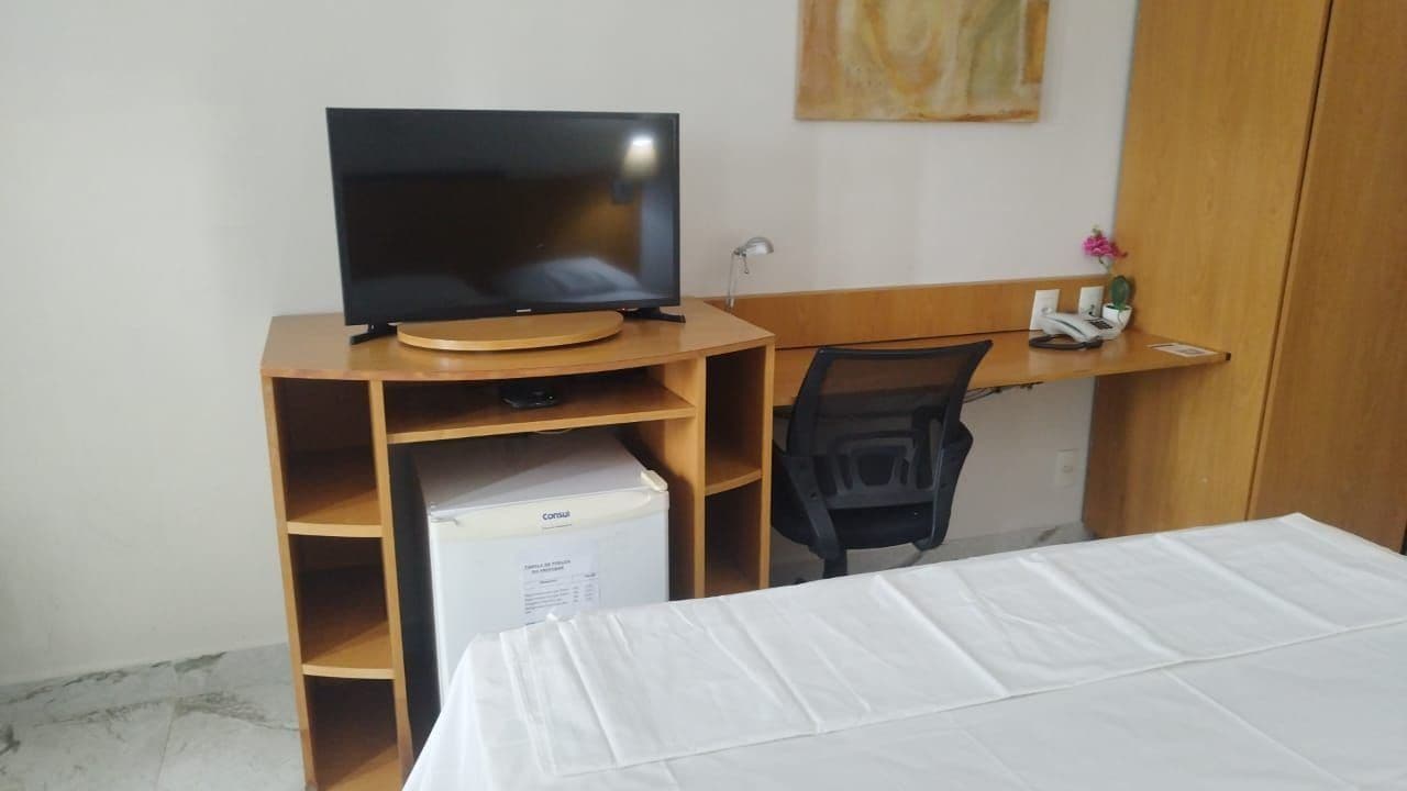 Una habitación de hotel con cama, escritorio con computadora, televisor y minibar.