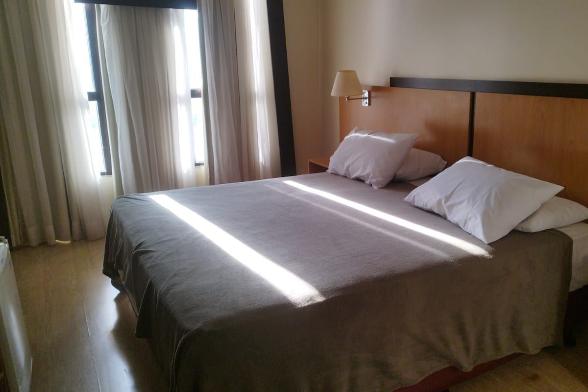 Une chambre d’hôtel avec un lit, des rideaux et une table de chevet.