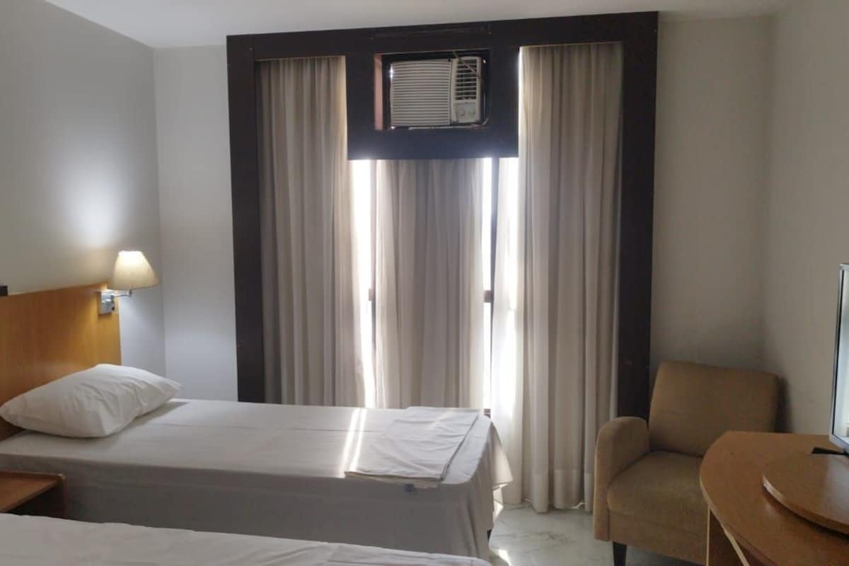 Une chambre d’hôtel avec deux lits, une télévision, une chaise et un appareil de climatisation.