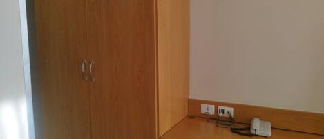 Una habitación con un armario de madera, un escritorio con teléfono y enchufes, y una silla.