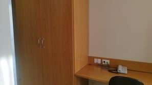 Une chambre avec une armoire en bois, un bureau doté d’un téléphone et de prises électriques.
