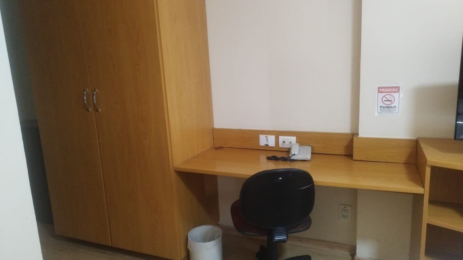 Un pequeño espacio de oficina con un escritorio de madera, una silla de oficina negra y un teléfono.