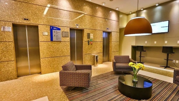 Un hall d'entrée doté de deux ascenseurs, de canapés à motifs, d'une table basse avec un vase et d'un téléviseur fixé au mur.