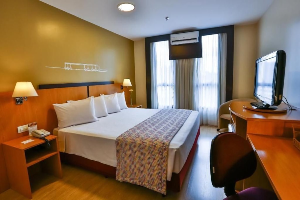 Une chambre d’hôtel équipée d’un lit, d’un bureau, d’une chaise, de lampes de chevet et d’un appareil de climatisation.
