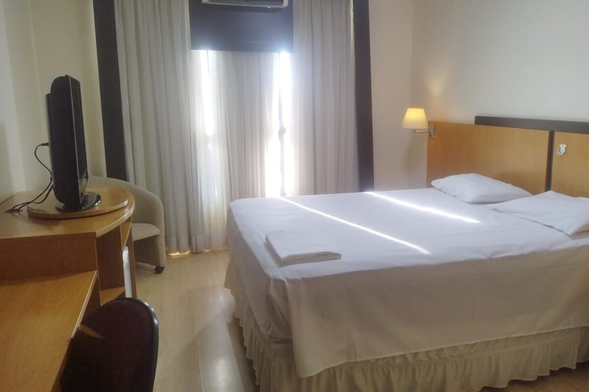 Une chambre d’hôtel avec un lit, un bureau, une chaise et un téléviseur.