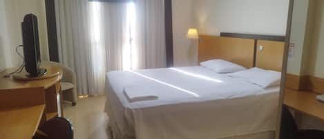 Una habitación de hotel con cama, escritorio, silla, televisor y lámpara.