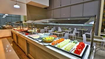 A buffet area with various food options, including fruits, vegetables, and prepared dishes, arranged on a counter with seating in the background.