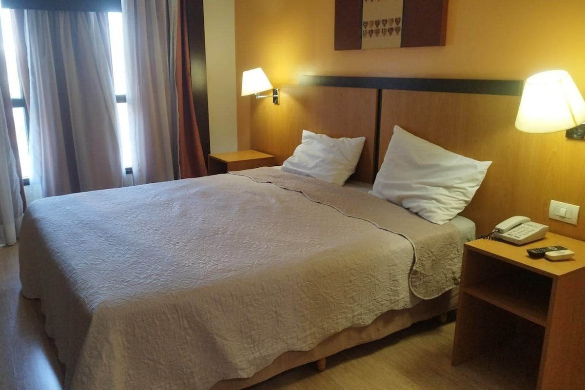 Une chambre d’hôtel avec un lit, deux lampes de chevet, une table de chevet avec un téléphone et un luminaire fixé au mur.
