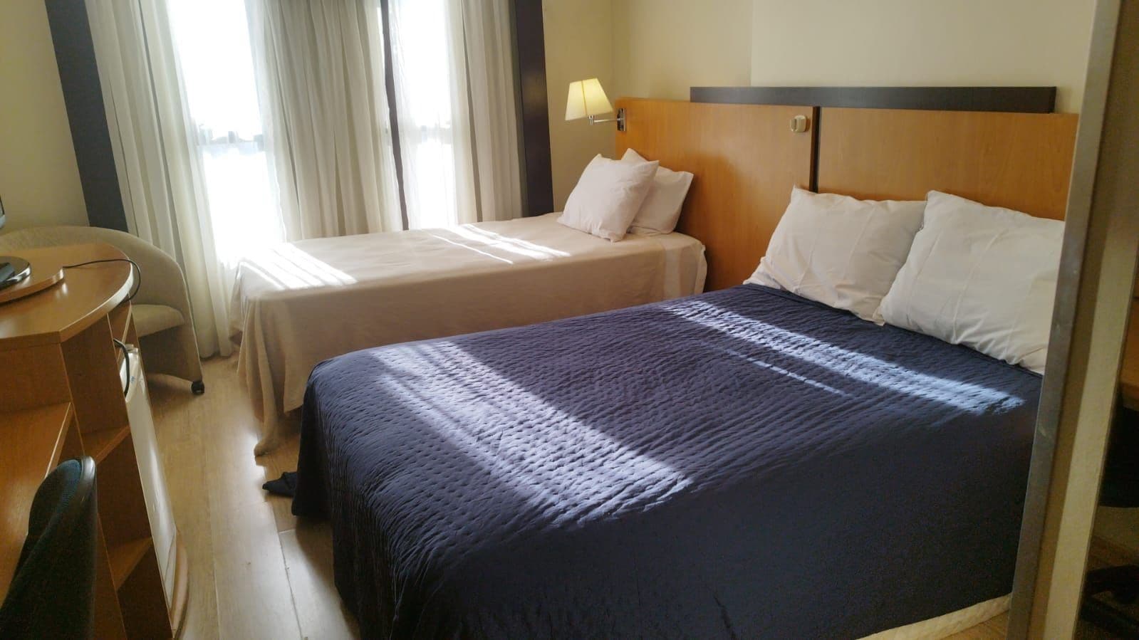 A hotel room with two beds, a desk, and a chair.