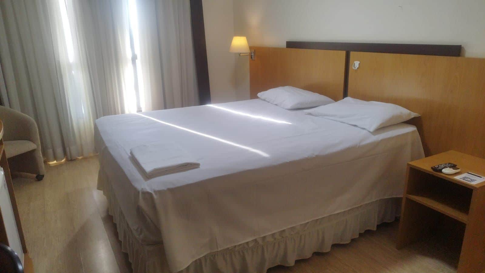 Una habitación de hotel con una cama grande, una mesita de noche con lámpara y una silla.