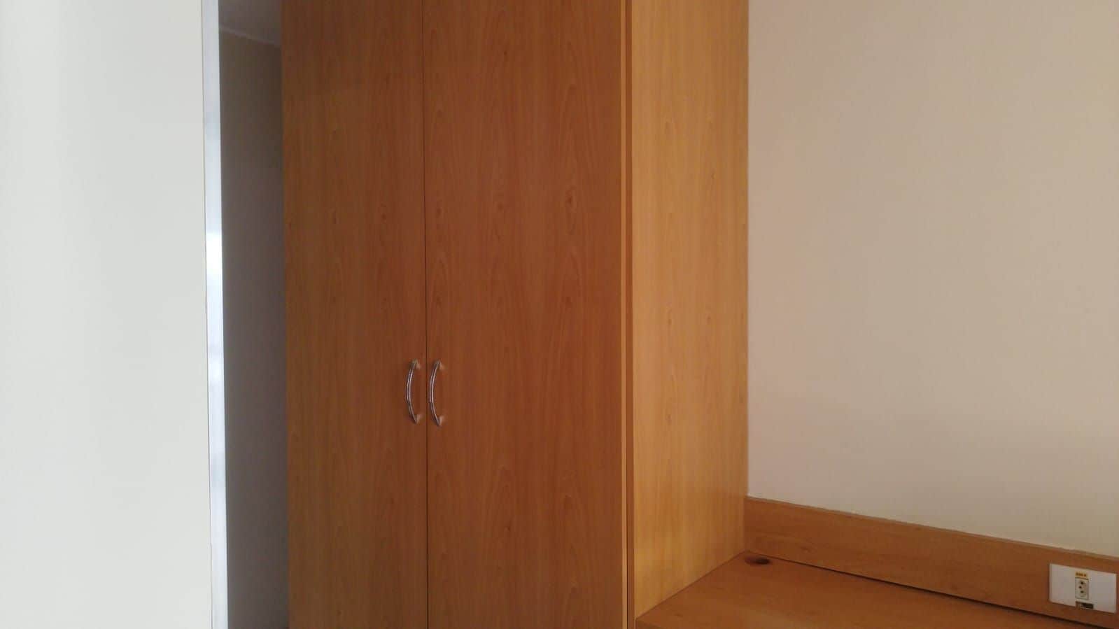 A wooden wardrobe with two handles, a white wall, and a wooden floor with a power outlet.