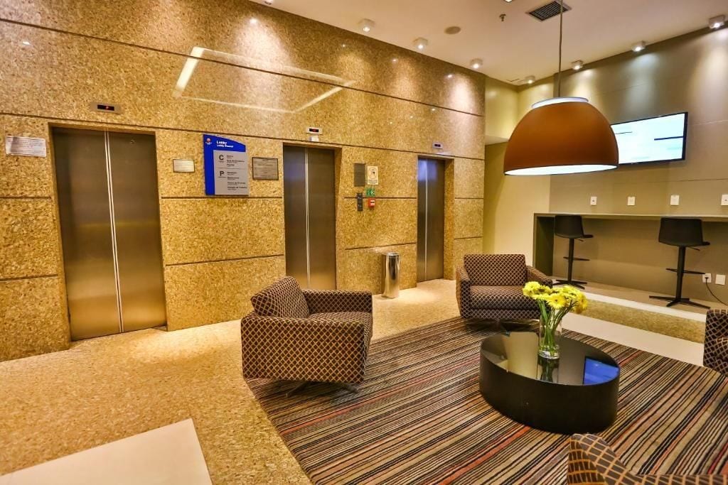A lobby with two elevators, patterned sofas, a coffee table with a vase, and a television mounted on the wall.